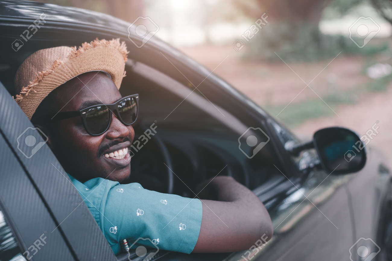 Happy african driver smiling while sitting in a car with open front window - 165592764 Happy african driver smiling while sitting in a car with open front window - 165592764