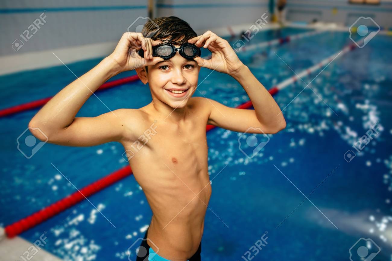 水泳を身に着けているフィットの若い男の子の肖像画は プールでゴーグルします 水着を着て微笑む少年スイマーの肖像画は スイミング プール でゴーグルします カメラ目線のプールで幸せなフィットの子 の写真素材 画像素材 Image