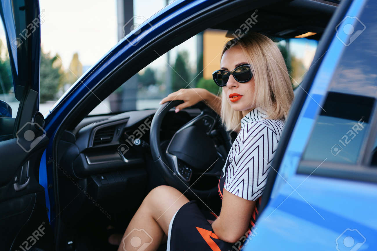 Confident and beautiful woman in sunglasses. Rear view of attractive young female in casual wear driving a car - 158991732 Confident and beautiful woman in sunglasses. Rear view of attractive young female in casual wear driving a car - 158991732