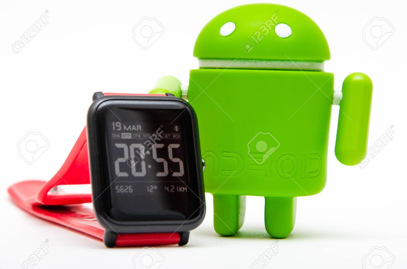 Android Figure And Tv Remote Green Plastic Figurine On A White Background Next To A Smart Watch With A Red Strap Clock On Android Smart Watch On A Mana S Hand Stock Photo