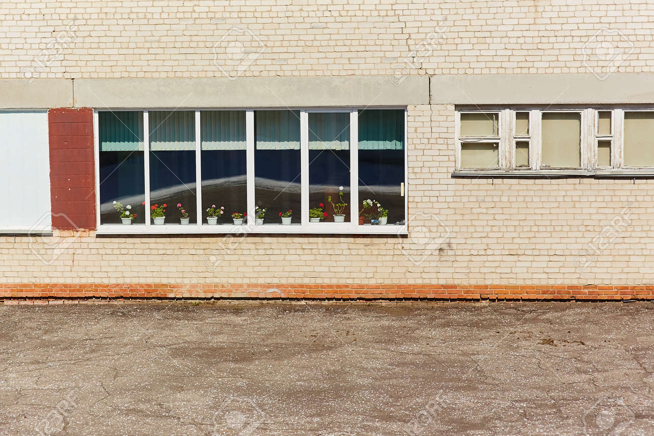 The wall of the old brick building, with a window with wooden frames, on the windowsill is blooming geranium. - 158596252 The wall of the old brick building, with a window with wooden frames, on the windowsill is blooming geranium. - 158596252