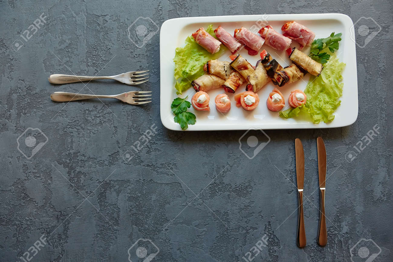 Three types of appetizers on a platter-mini canapes of red fish, eggplant rolls and ham with filling, on a beautiful gray background with forks. Place for copy space. - 158596256 Three types of appetizers on a platter-mini canapes of red fish, eggplant rolls and ham with filling, on a beautiful gray background with forks. Place for copy space. - 158596256