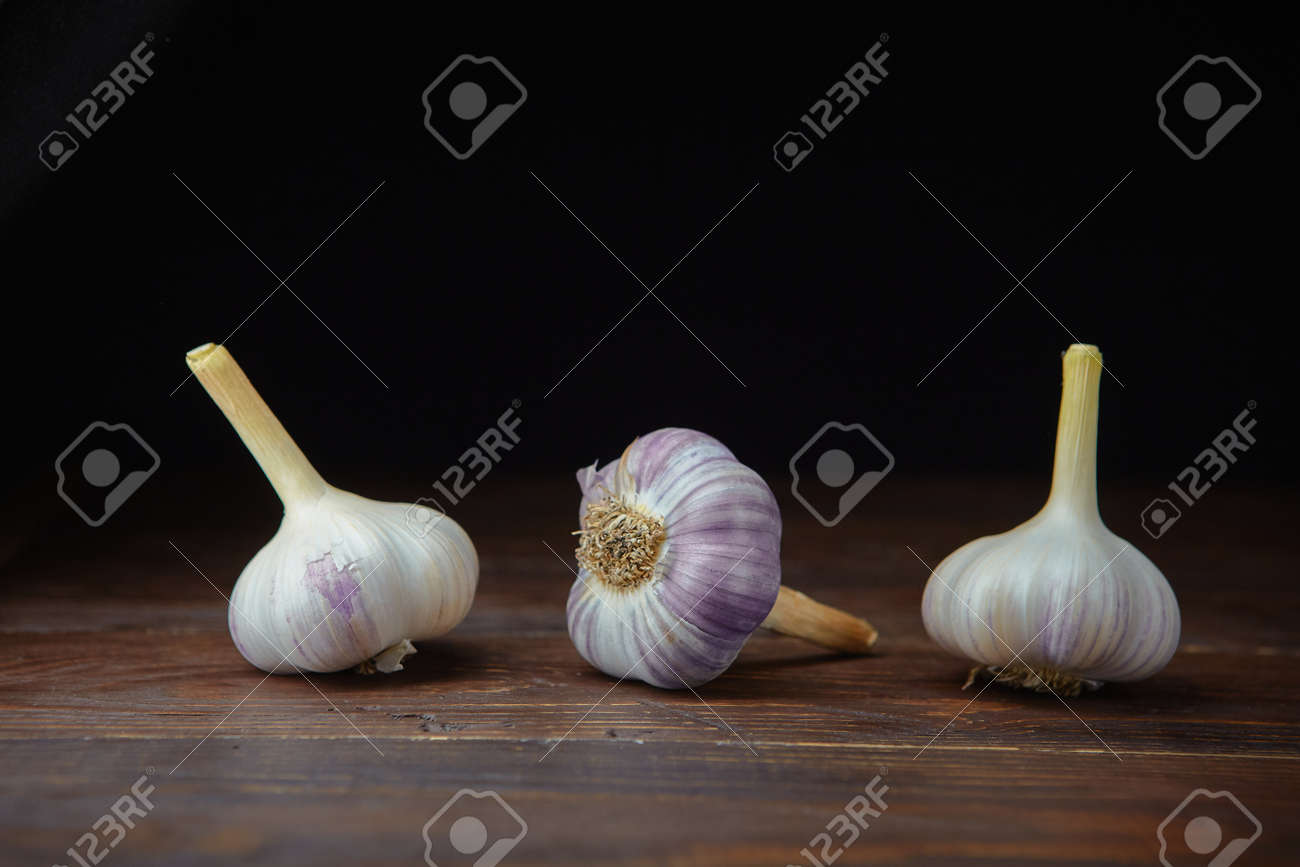 Three ripe heads of fresh garlic on a dark wooden background. Folk medicine for viral and colds. - 158596260 Three ripe heads of fresh garlic on a dark wooden background. Folk medicine for viral and colds. - 158596260