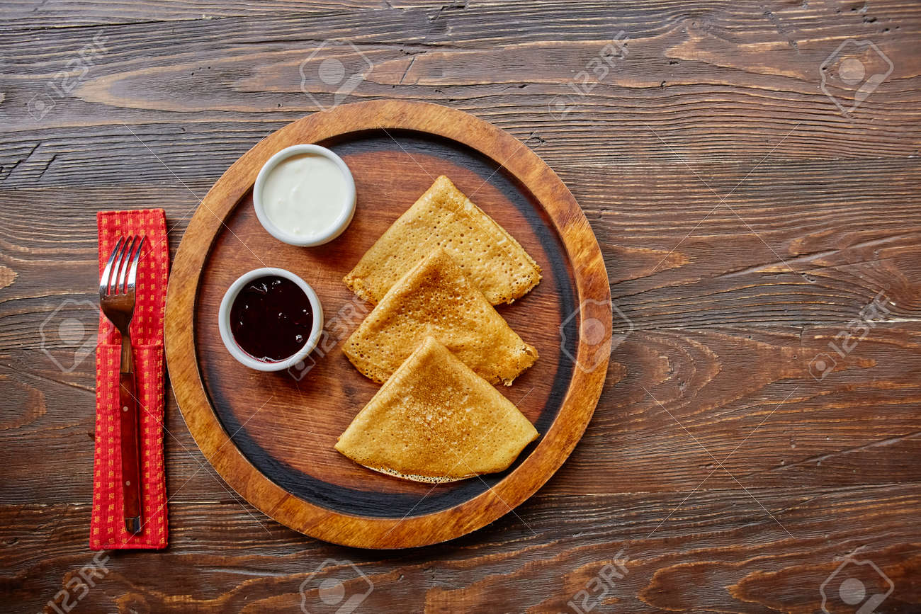 Homemade hot delicious pancakes with sour cream and jam on a wooden plate, top view - 158618865 Homemade hot delicious pancakes with sour cream and jam on a wooden plate, top view - 158618865