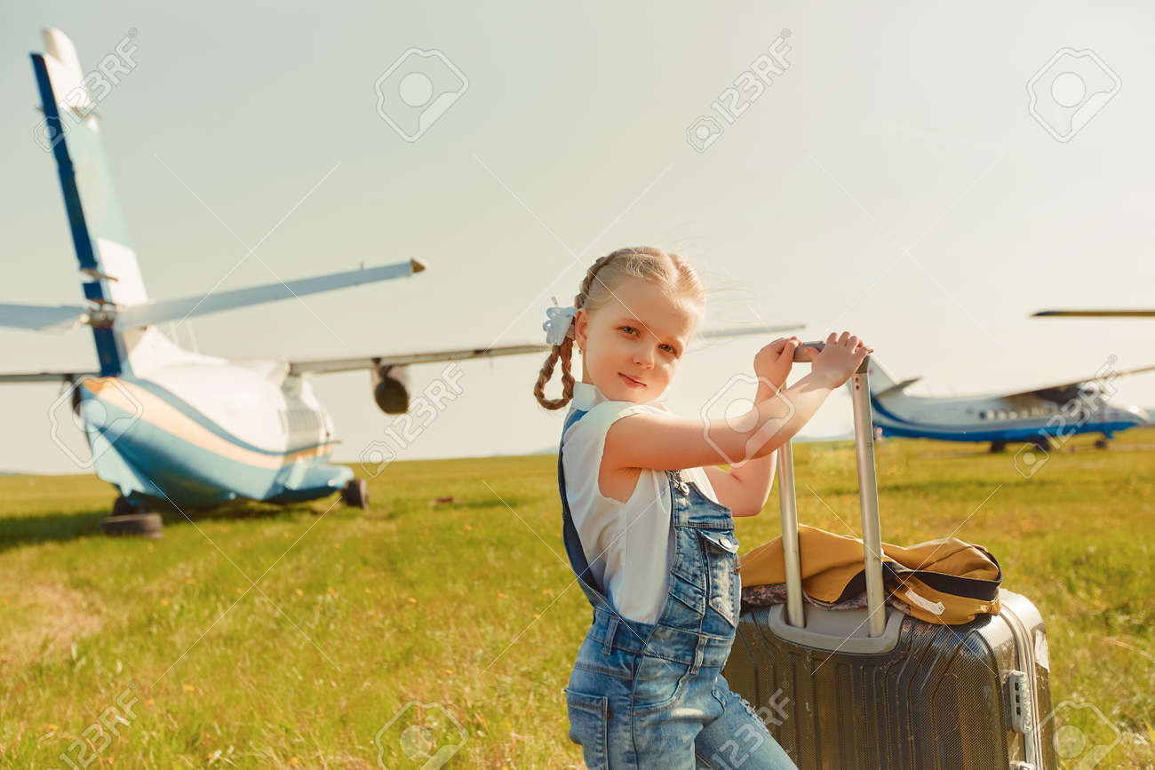 A little girl with a suitcase on the tarmac is going to travel by plane. - 158561424 A little girl with a suitcase on the tarmac is going to travel by plane. - 158561424