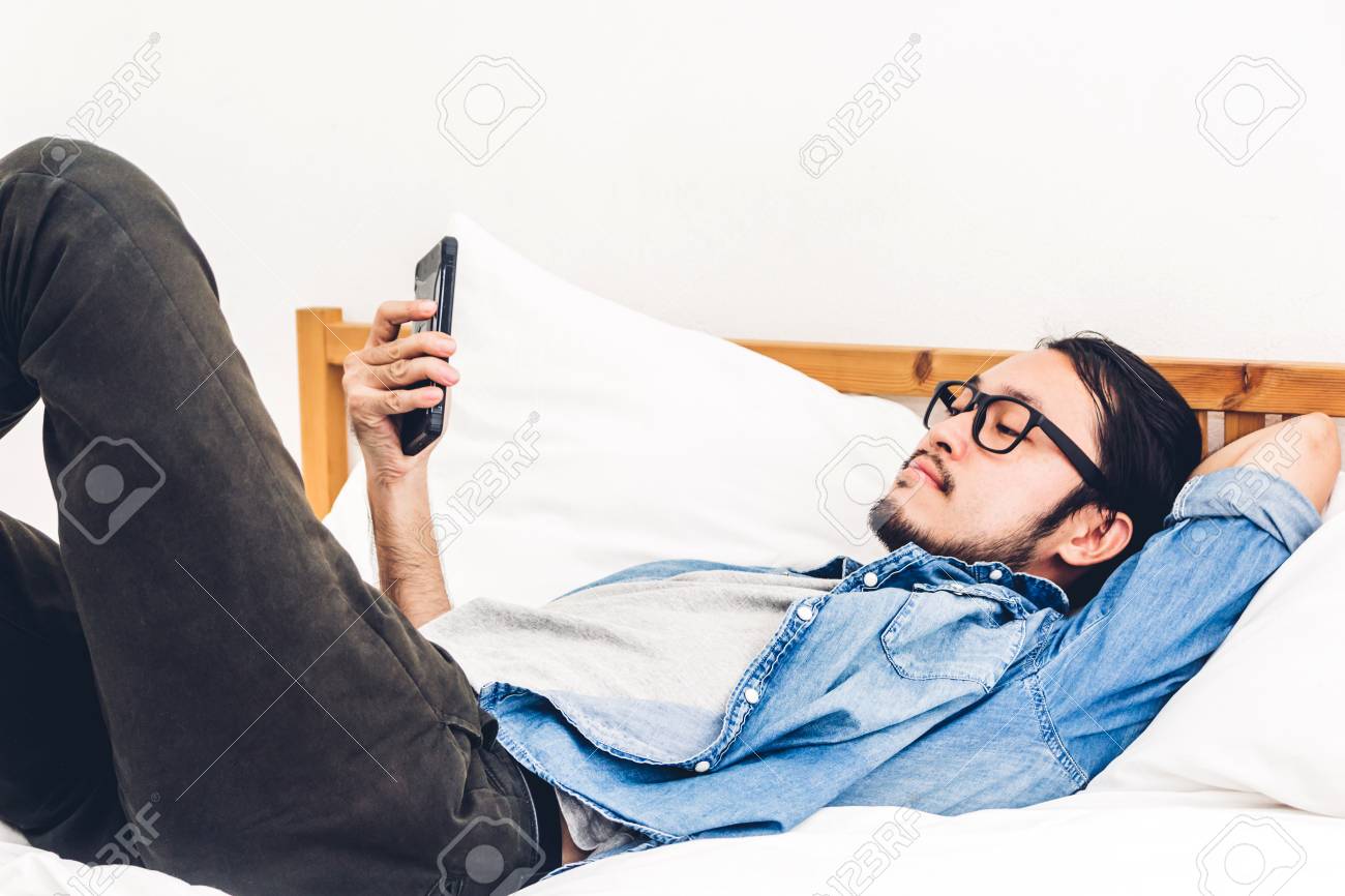 Man relaxing using and talking by smartphone on the bed at home.technology and communication concept - 109078230 Man relaxing using and talking by smartphone on the bed at home.technology and communication concept - 109078230