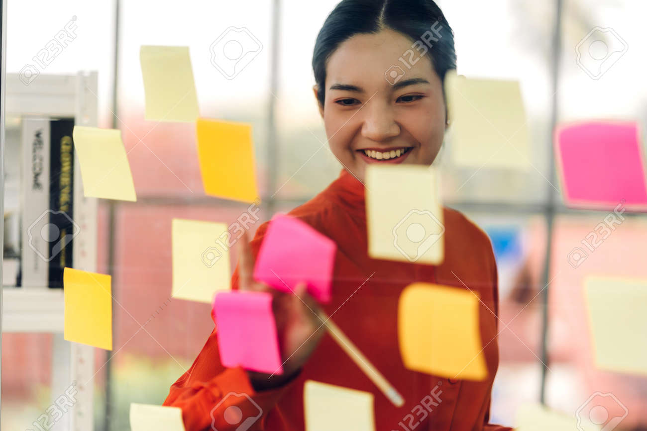 Casual business woman planning and working writing over the project with stickers note on glass window at modern office - 168607223 Casual business woman planning and working writing over the project with stickers note on glass window at modern office - 168607223