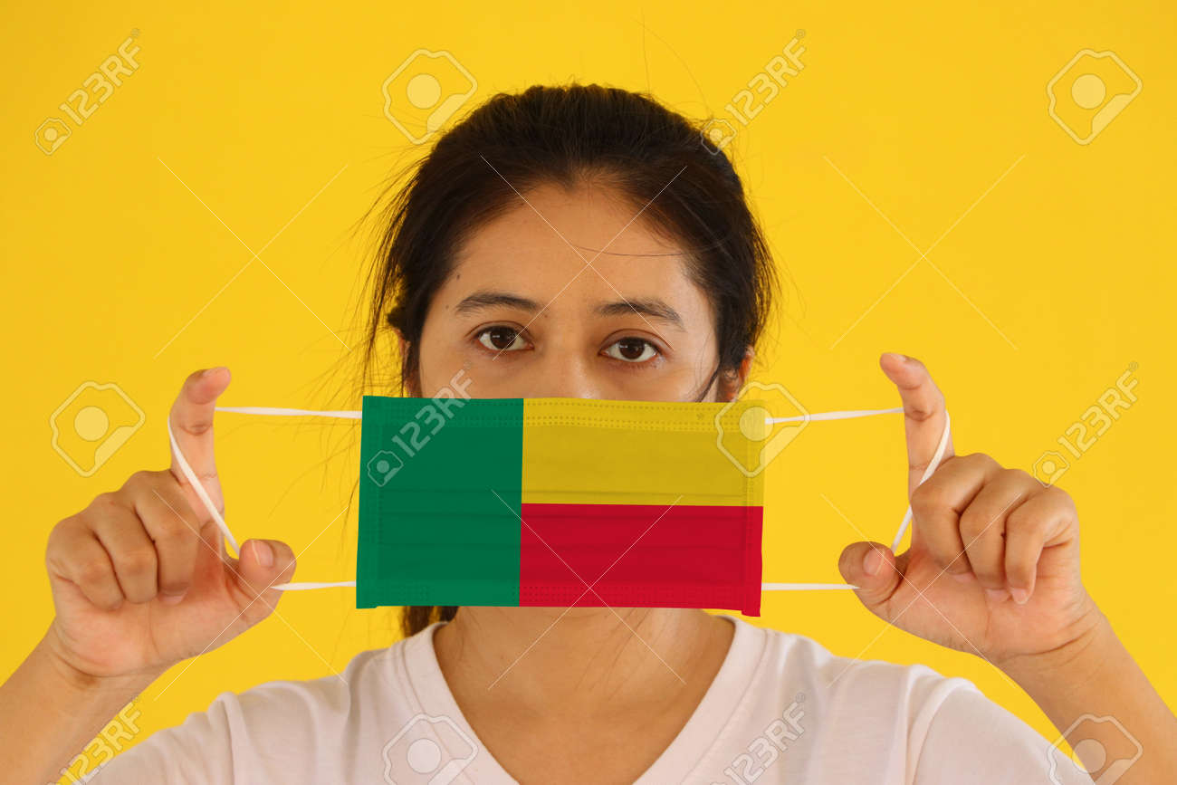 A woman in white shirt with Benin flag on hygienic mask in her hand and lifted up the front face on yellow background. Tiny Particle or virus corona or Covid 19 protection. Concept of Combating illness. - 158803112 A woman in white shirt with Benin flag on hygienic mask in her hand and lifted up the front face on yellow background. Tiny Particle or virus corona or Covid 19 protection. Concept of Combating illness. - 158803112
