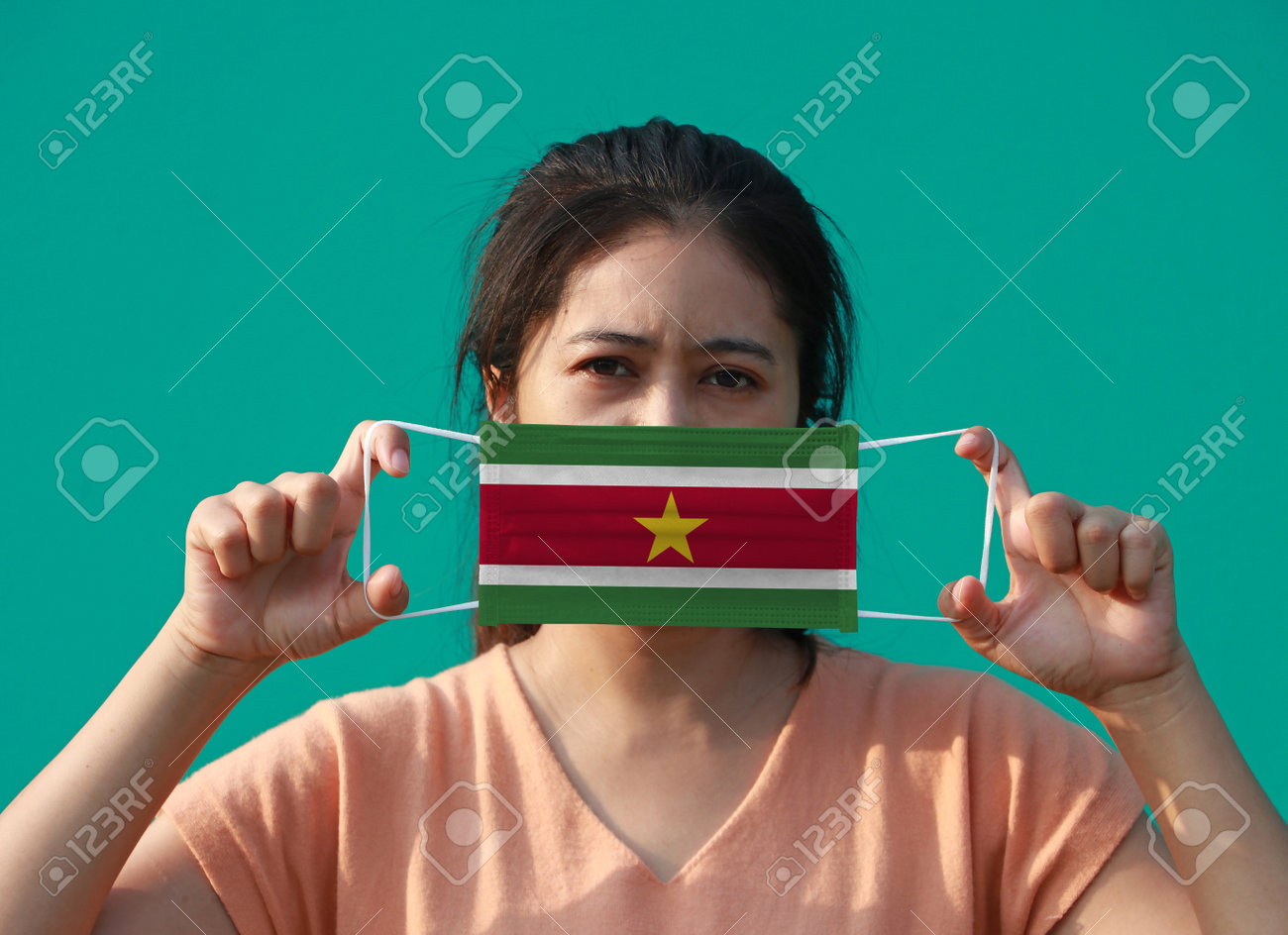 A woman with Suriname flag on hygienic mask in her hand and lifted up the front face on green background. Tiny Particle or virus corona or Covid 19 protection. Concept of Combating illness. - 160156377 A woman with Suriname flag on hygienic mask in her hand and lifted up the front face on green background. Tiny Particle or virus corona or Covid 19 protection. Concept of Combating illness. - 160156377