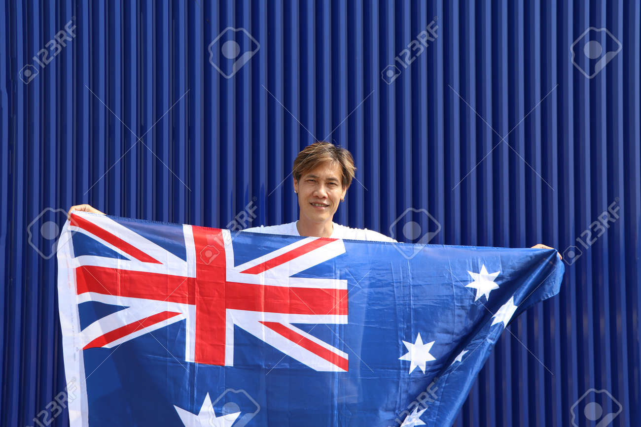 The man is holding Australia fabric flag in his hands on blue background. - 163875071 The man is holding Australia fabric flag in his hands on blue background. - 163875071