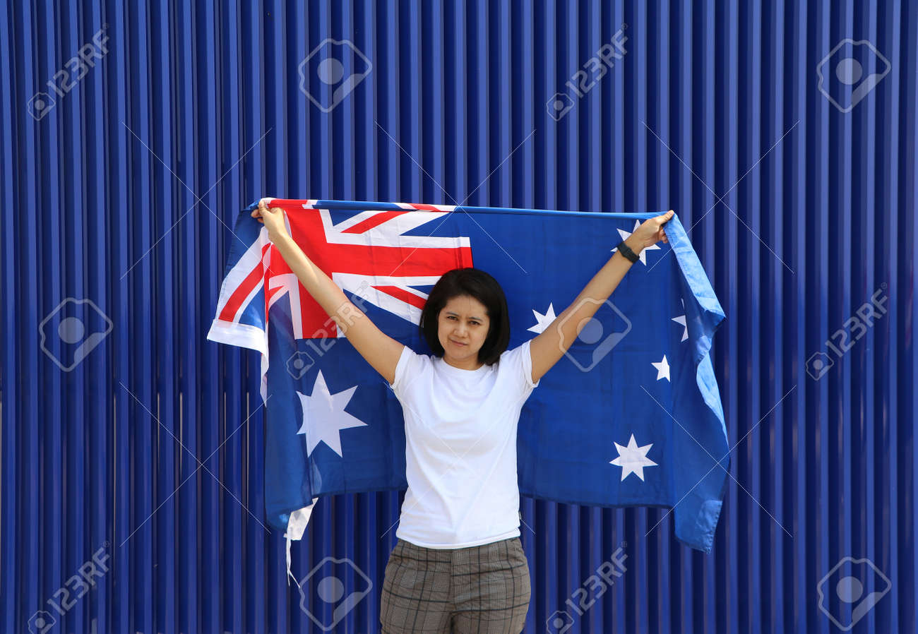 pretty lady is holding Australia flag in her hands and raising to the end of the arm at the back on blue background. - 163875073 pretty lady is holding Australia flag in her hands and raising to the end of the arm at the back on blue background. - 163875073