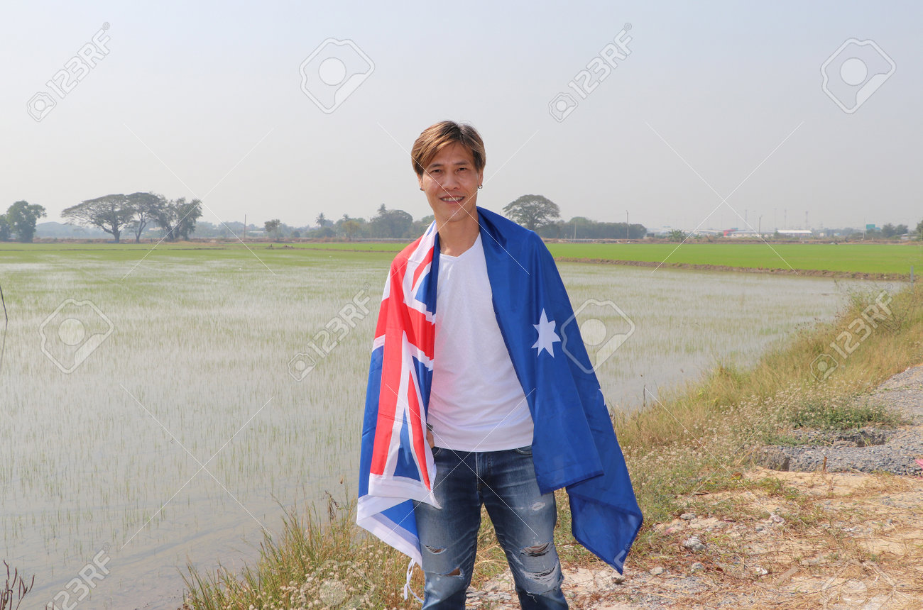 The man in white shirt with Australia flag on his shoulder on nature view and rice fields background. - 164472049 The man in white shirt with Australia flag on his shoulder on nature view and rice fields background. - 164472049