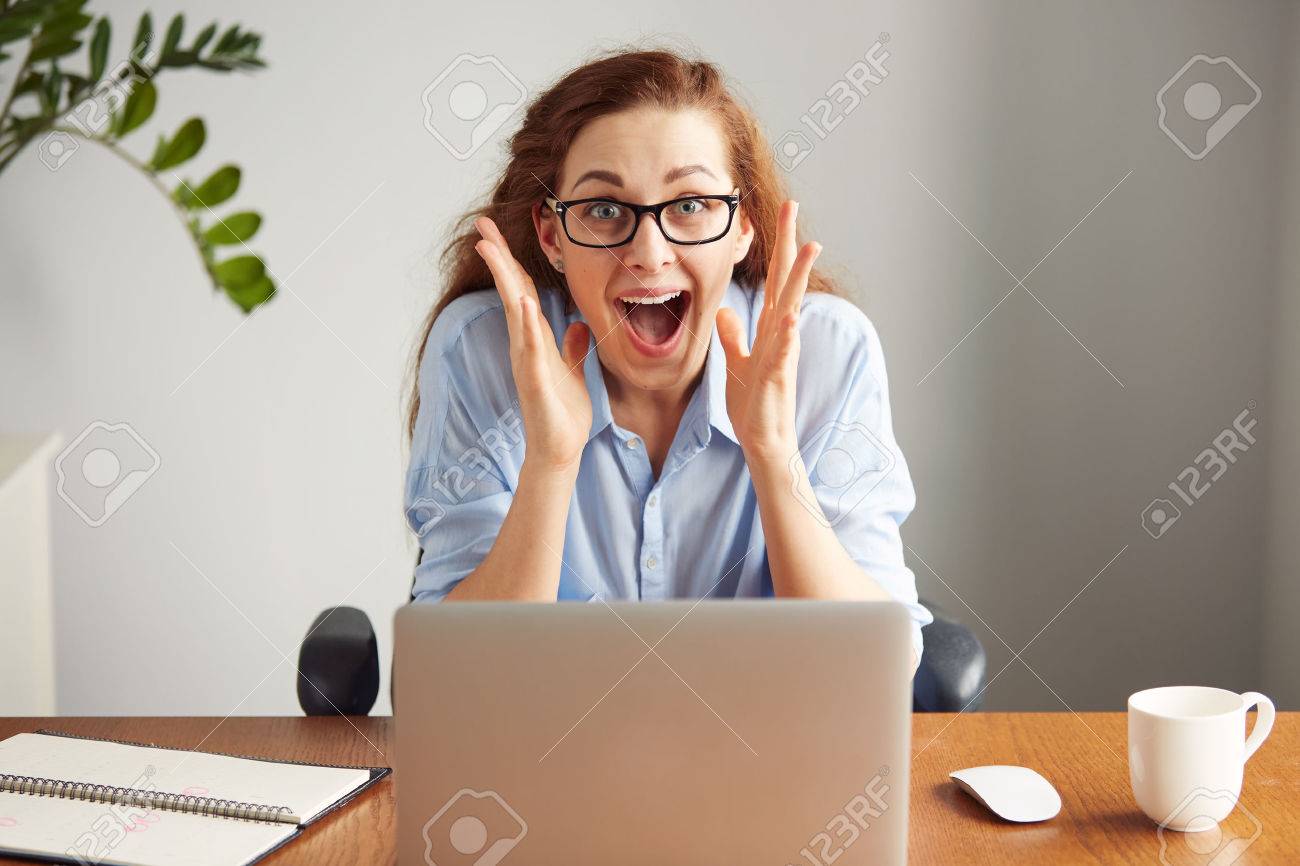 Portrait of a cute redhead girl wearing glasses and blue shirt screaming with excitement and joy while working on her laptop. Headshot of an excited female student with winning expression on her face - 55379315 Portrait of a cute redhead girl wearing glasses and blue shirt screaming with excitement and joy while working on her laptop. Headshot of an excited female student with winning expression on her face - 55379315
