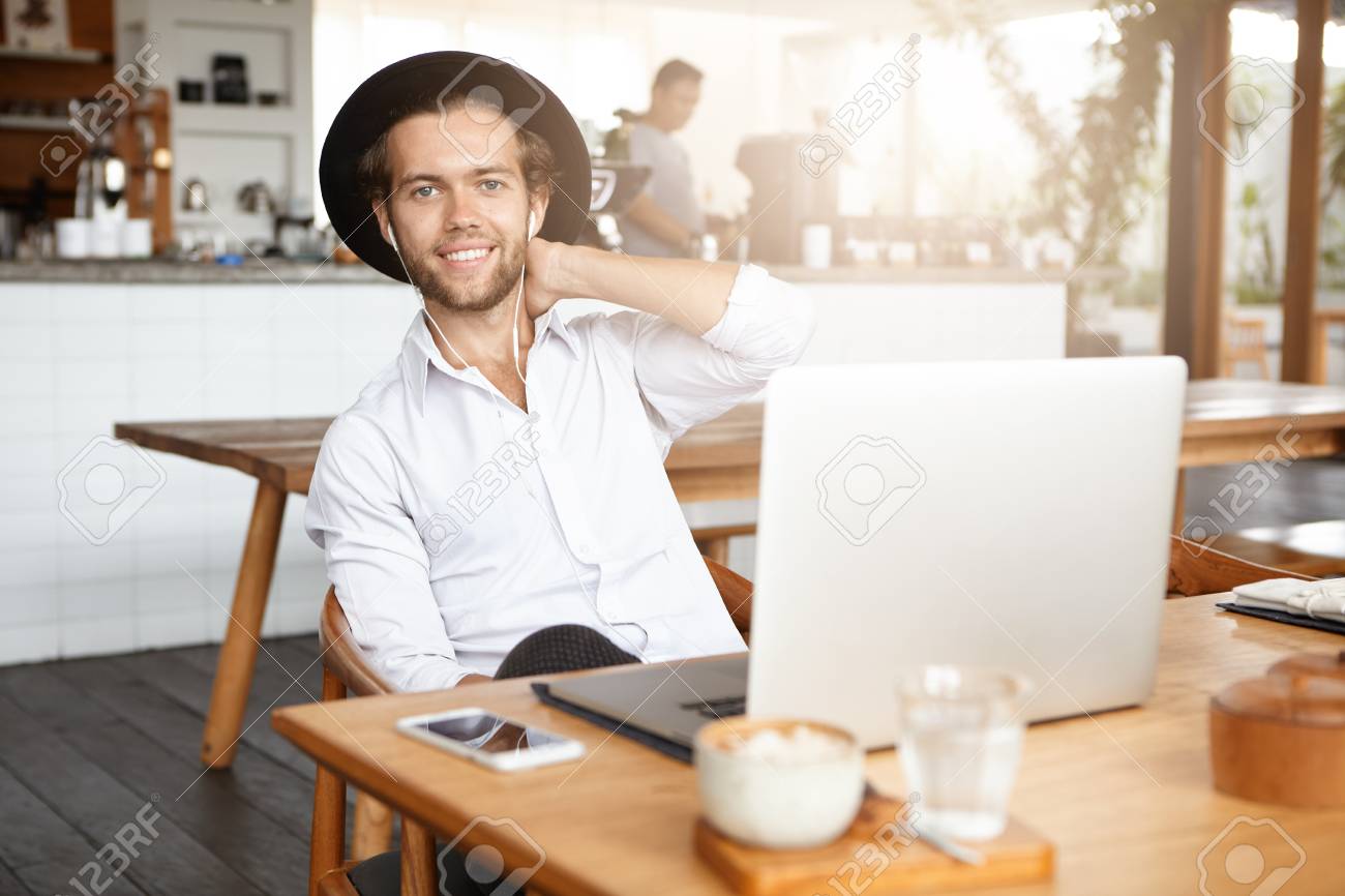 技術は 生活を容易になります おしゃれなひげを生やした男性無料ワイヤレス インター ネット接続を使用して 自分のラップトップ上のイヤホンで聴いている音楽やオーディオ ブックをオンラインの昼食時にモダンなカフェのインテリア の写真素材 画像素材 Image