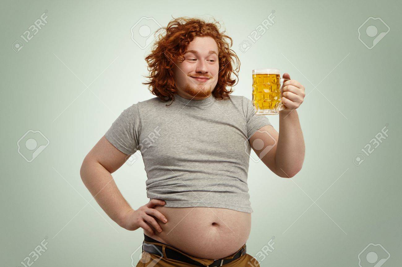 Heureux Homme En Surpoids Rousse Avec Gros Ventre Qui Sort De Son T Shirt Retracte Tenant Un Verre De Biere Froide Regardant Dans L Anticipation Impatient De Sentir Son Bon Gout Tout En Se
