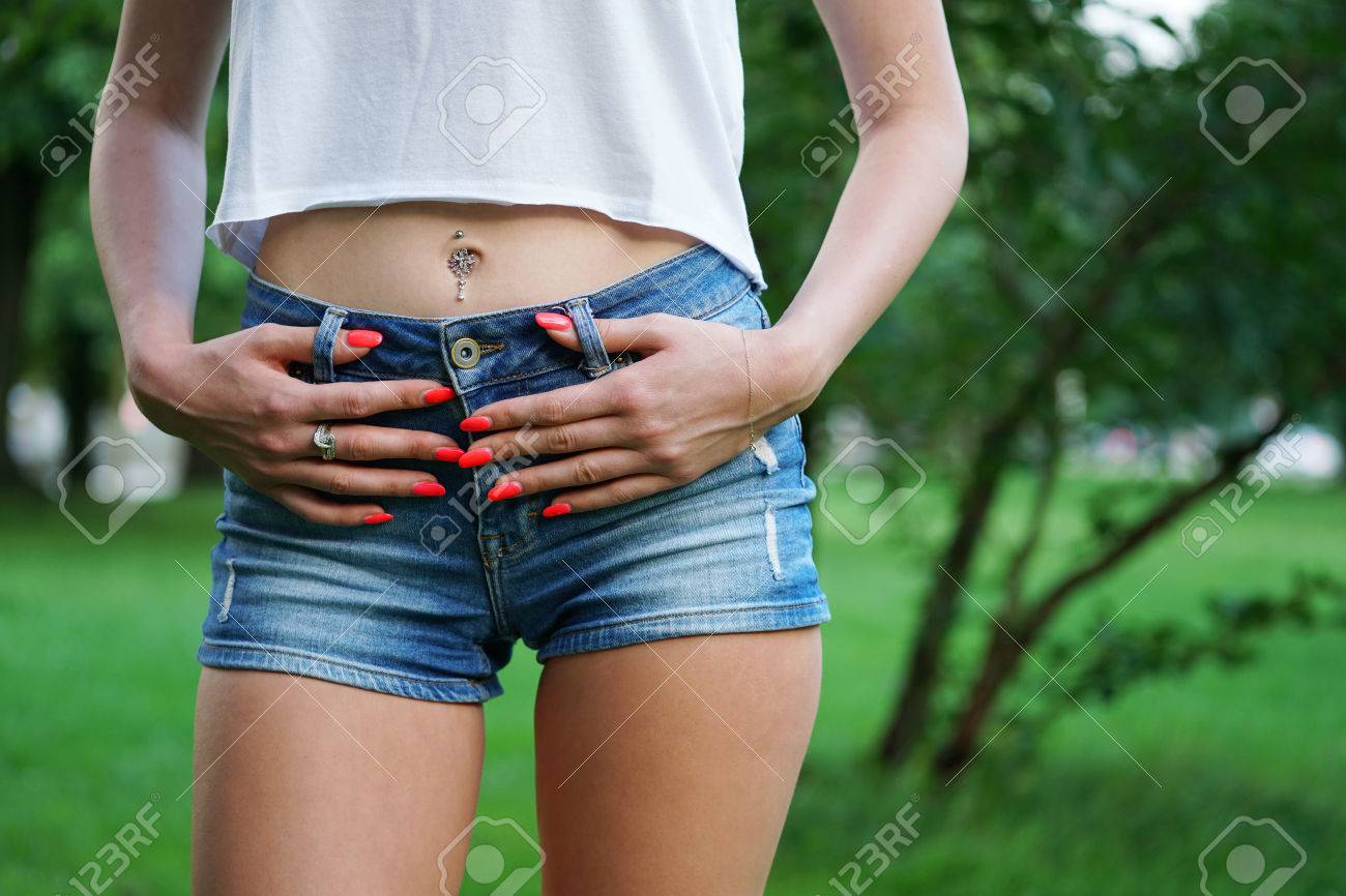 デニム ホットパンツまたは戦利品ショート パンツ へそピアスとオレンジのマニキュアを着た若い女性の中間セクション ファッションのトレンド の写真素材 画像素材 Image
