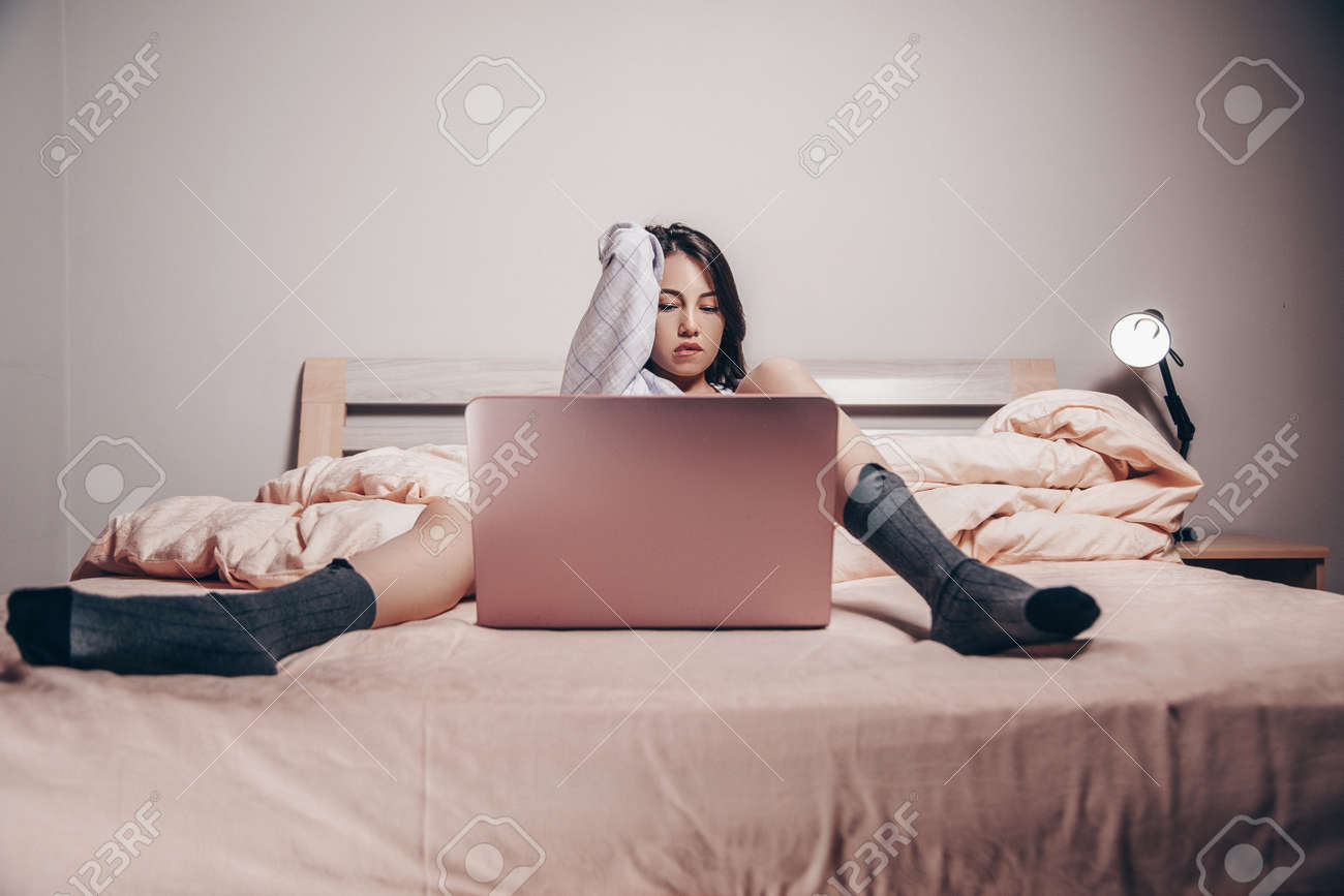 A Young Asian Webcam Model Girl Is Lying In Front Of A Laptop With Her Legs  Spread. Enjoys And Shows Her Charms. Low Depth Of Focus, Selective Focus.  Stock Photo, Picture and