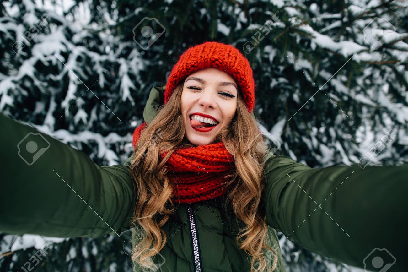 冬の自分撮り 赤いニット帽子とスカーフの若い幸せな女の子は自分撮りを取り 冬の寒い日に猿を再生します 女の子は冬の自分撮りを取ります の写真素材 画像素材 Image