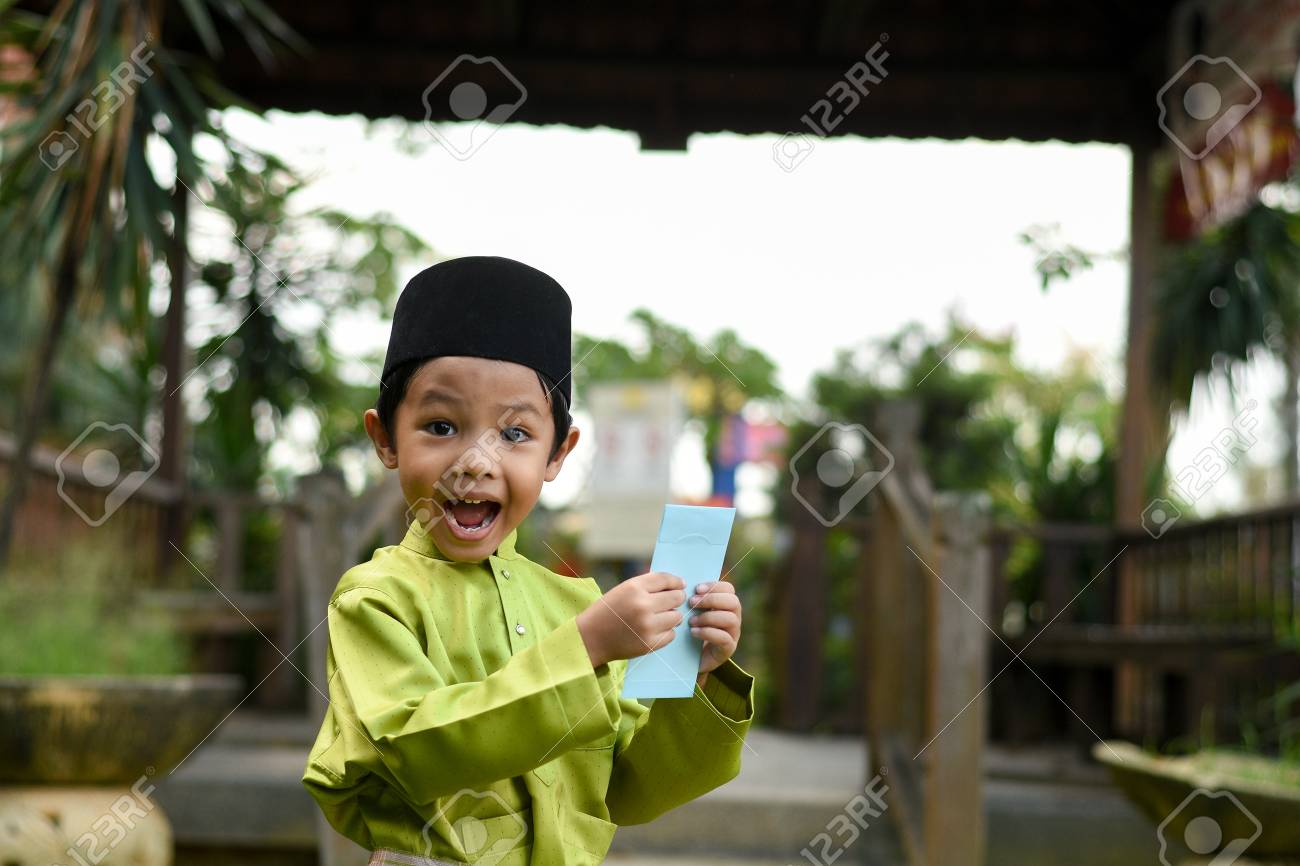 A Malay boy in Malay traditional cloth showing his happy reaction after received money pocket during Eid Fitri or Hari Raya celebration. - 102639558 A Malay boy in Malay traditional cloth showing his happy reaction after received money pocket during Eid Fitri or Hari Raya celebration. - 102639558