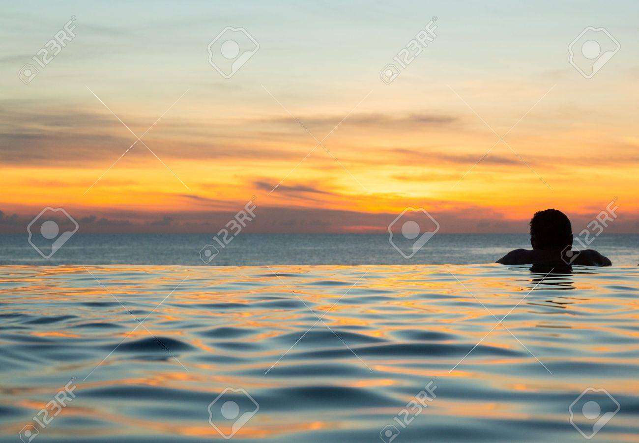 夕暮れの海を一望できるインフィニティ スイミング プールの端に人の頭のシルエット の写真素材 画像素材 Image