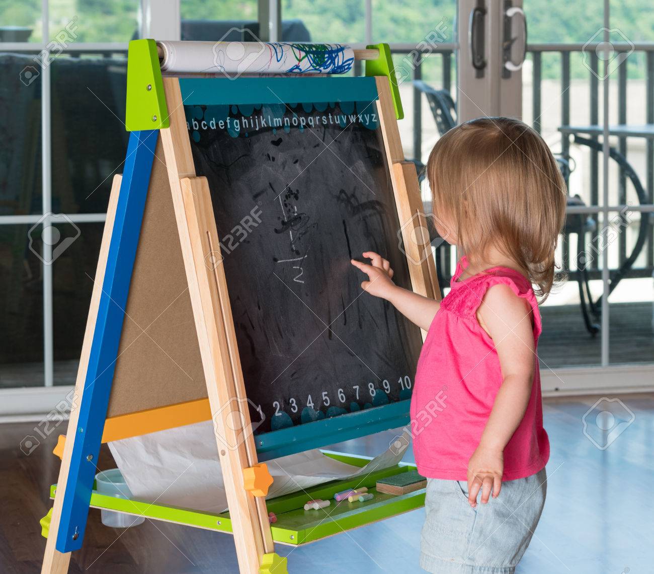 young two year old girl drawing with finger on blackboard on stock