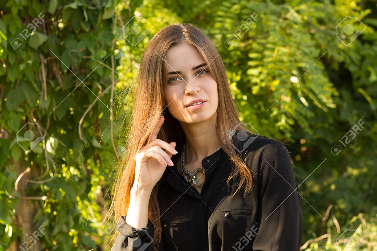 Bonita Joven Con El Pelo Largo Marrón En Blusa Negra Y Collar De Plata En El Fondo De árboles Verdes Y Luz Del Sol Brillante Fotos, Retratos, Imágenes Y Fotografía De