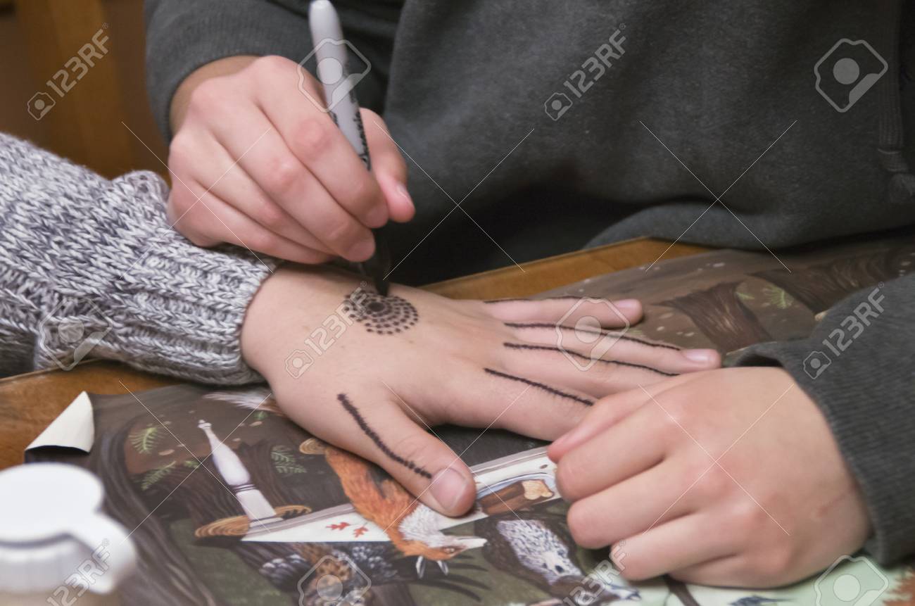A Young Lady Uses A Pen To Draw A Design On The Hand Of A Girl