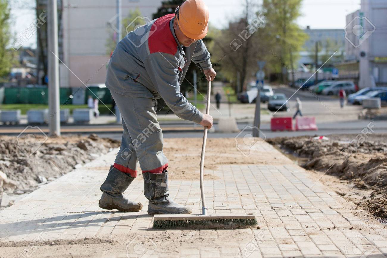 Construction worker grouting dry sand with brush into paver bricks joints during road works - 55641666 Construction worker grouting dry sand with brush into paver bricks joints during road works - 55641666