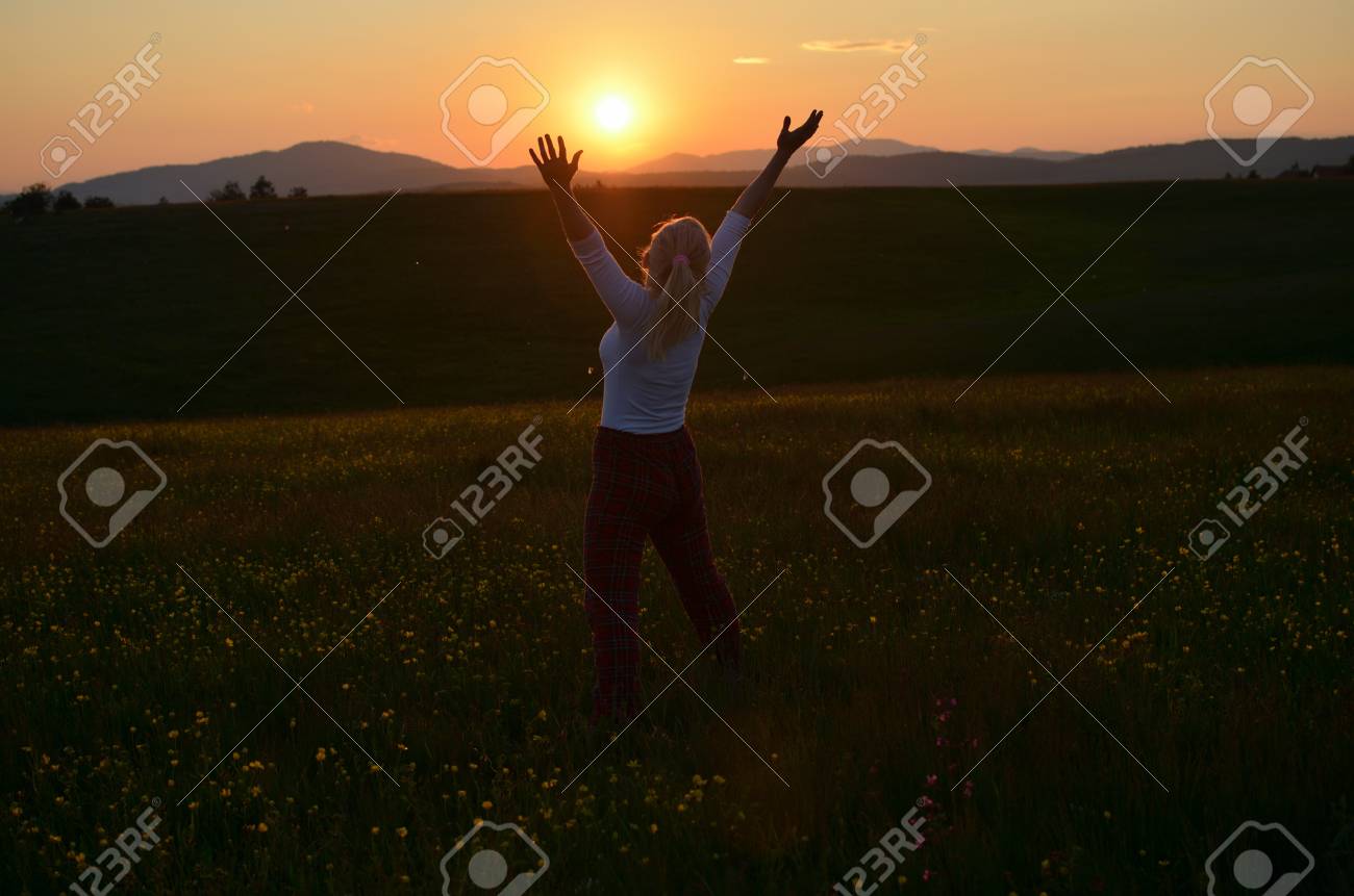 日没の太陽丘に向かって両手を広げるポーズでうれしそうな雰囲気の女性 の写真素材 画像素材 Image