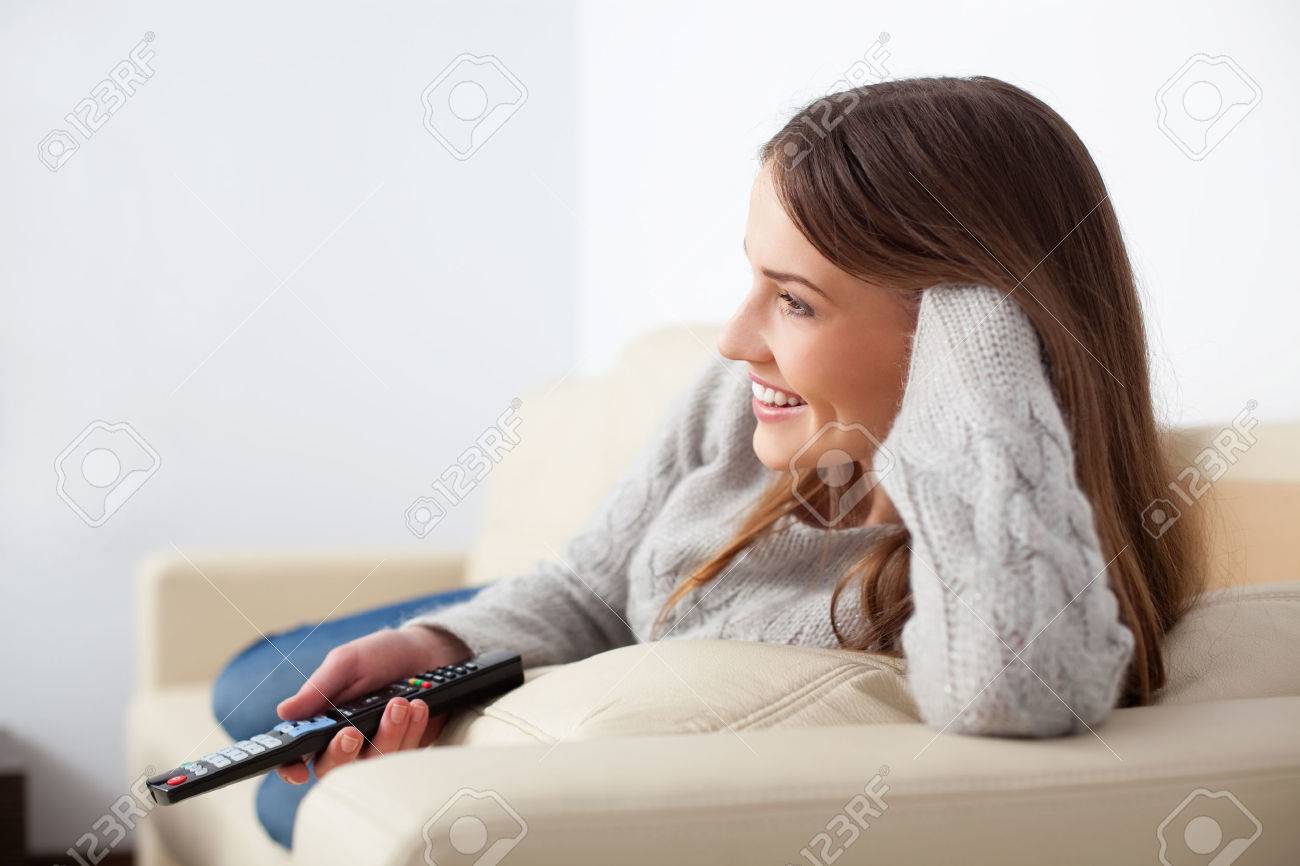 Happy young woman watching tv on sofa - 53950960 Happy young woman watching tv on sofa - 53950960