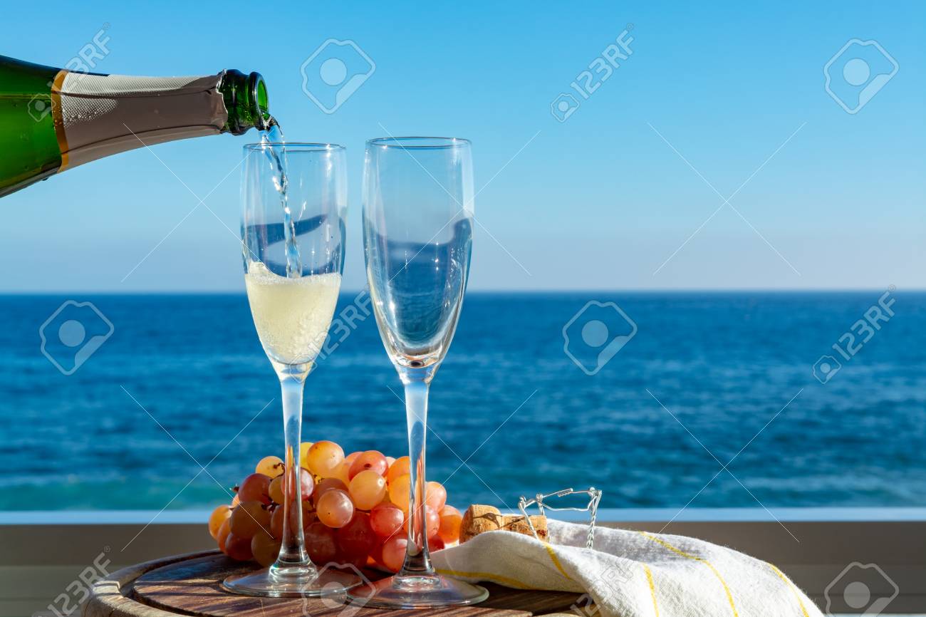 Waiter pouring Champagne, prosecco or cava in two glasses on outside terrace with sea view close up - 113774086 Waiter pouring Champagne, prosecco or cava in two glasses on outside terrace with sea view close up - 113774086