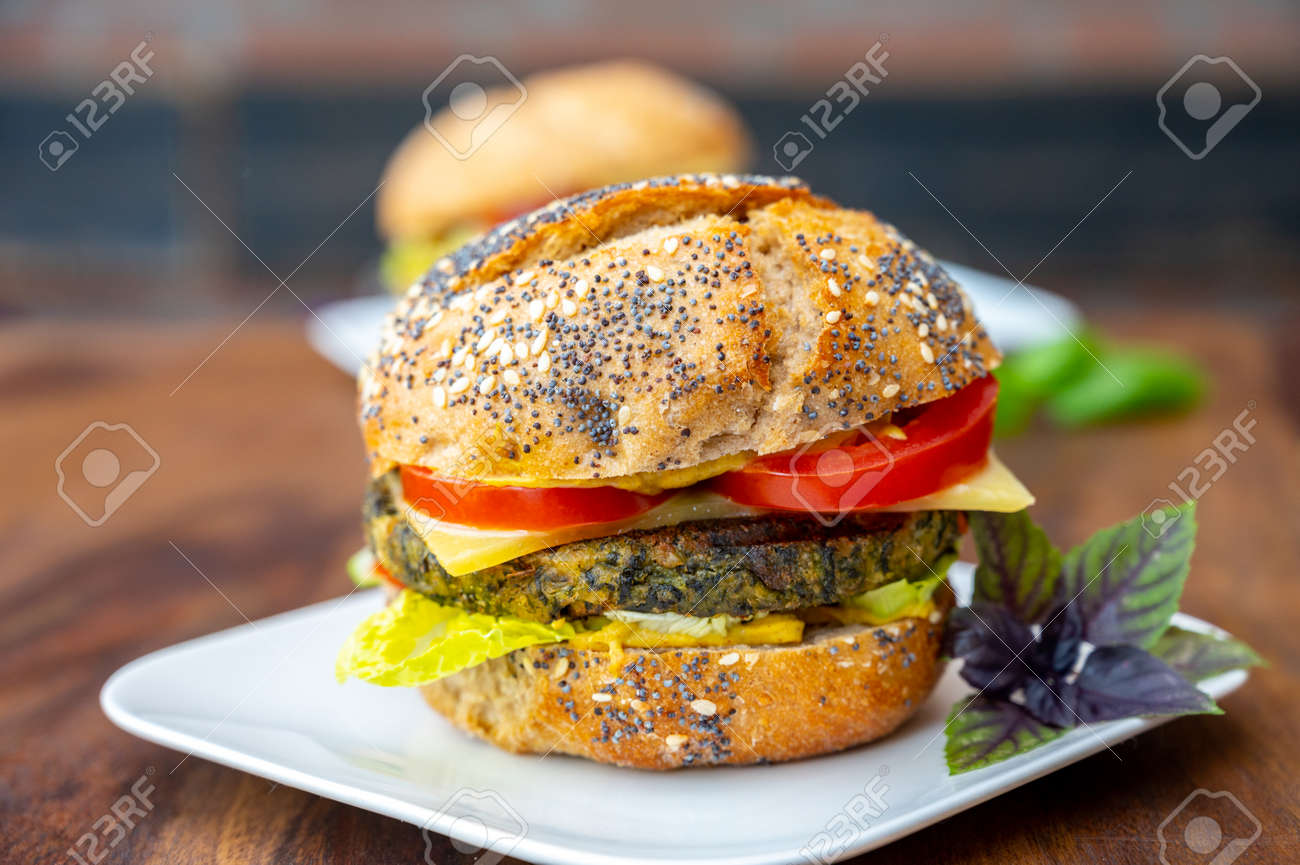 Eating of fresh and healthy vegetarian burgers with grilled spinach or pumpkin burgers, organic buns and vegetables close up - 155595771 Eating of fresh and healthy vegetarian burgers with grilled spinach or pumpkin burgers, organic buns and vegetables close up - 155595771