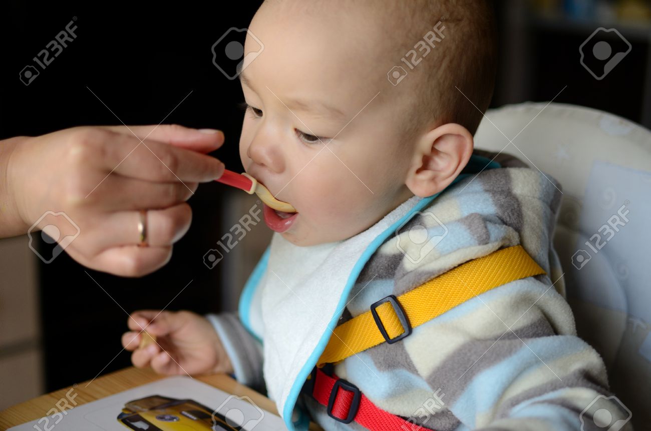 mother is feeding small baby boy child eats from the spoon stock