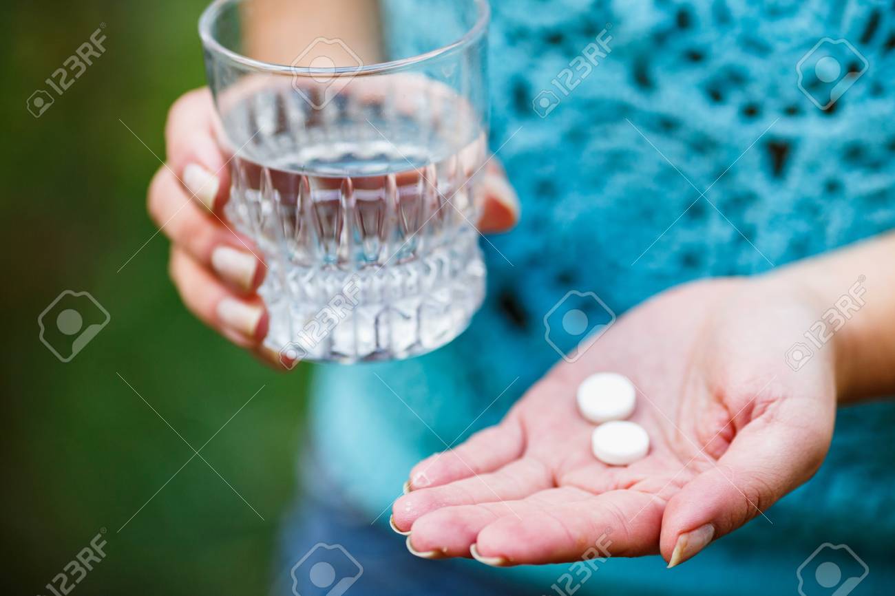 the girl holds a glass of clean water and two white pills - 97368613 the girl holds a glass of clean water and two white pills - 97368613