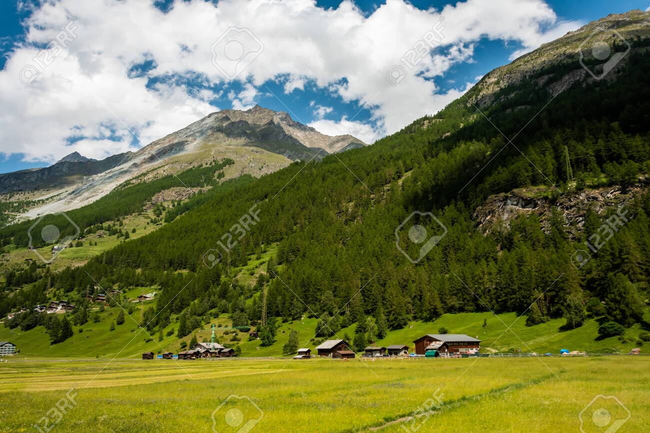 A Small Village At The Foot Of The Mountain In The Swiss Alps. View Of The  Green Slope In The Mountains. Idyllic Outdoor Scene In Switzerland, Europe  Stock Photo, Picture and Royalty