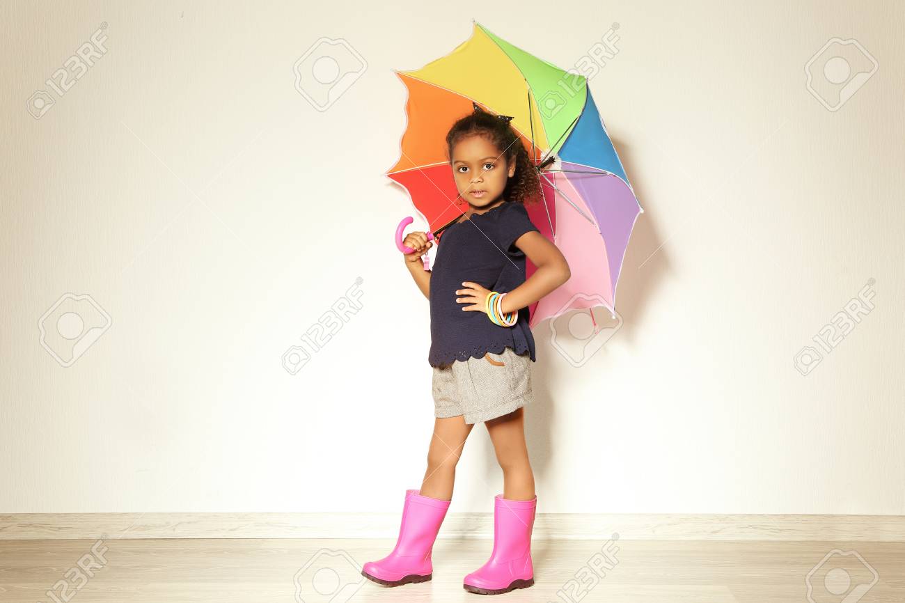 軽い壁に対してゴムブーツに傘を持つかわいいアフリカ系アメリカ人の女の子 ファッションコンセプト の写真素材 画像素材 Image