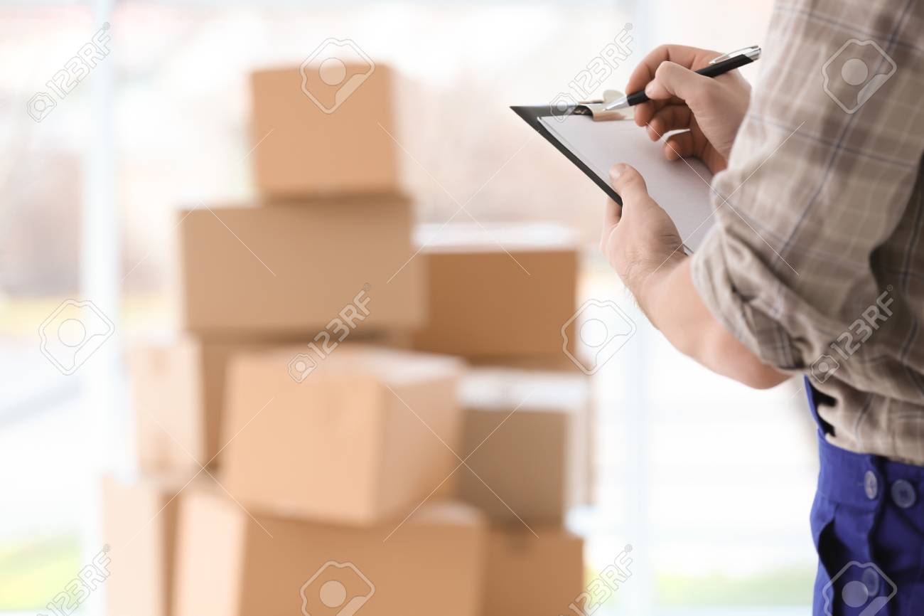 Man holding clipboard on blurred boxes background - 97297311 Man holding clipboard on blurred boxes background - 97297311