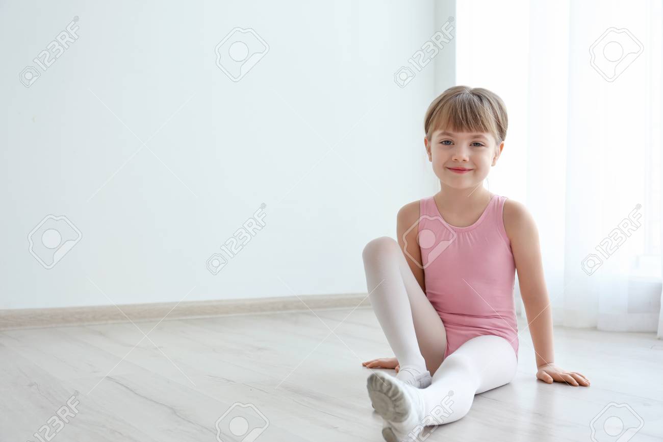 Cute Little Ballerina Sitting On Floor In Dance Studio Stock Photo