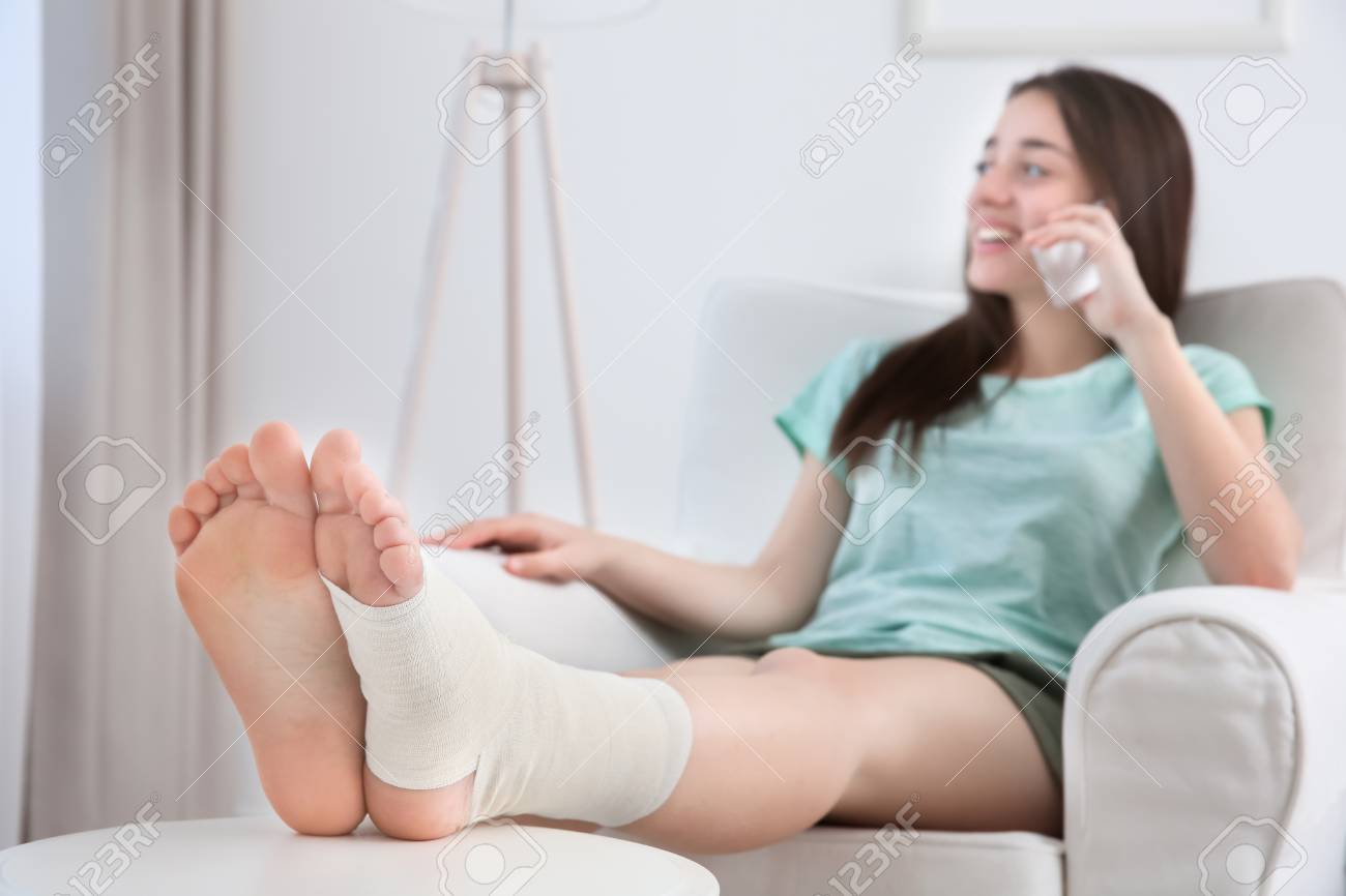 Beautiful Young Woman With Bandaged Leg Talking By Mobile Phone While Sitting In Arm-chair At Home Stock Photo, Picture And Royalty Free Image. Image 98218997.