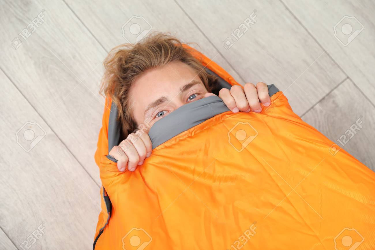 Young Man In Comfortable Sleeping Bag On Floor Top View Stock