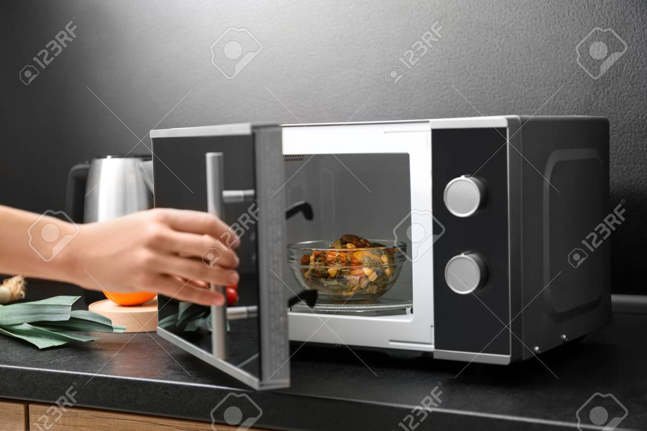 Young Woman Using Microwave Oven On Table In Kitchen - 