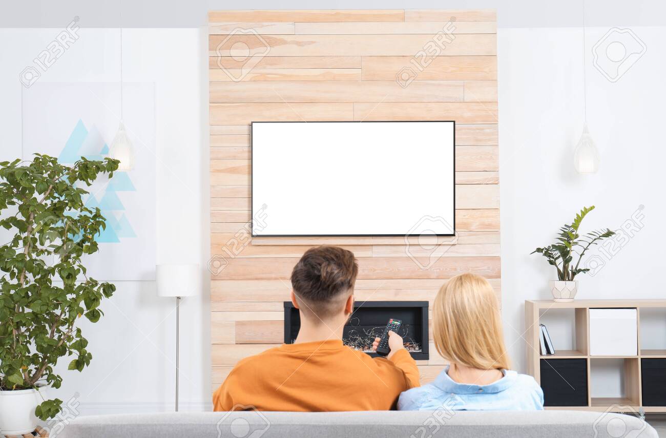 Couple watching TV on sofa in living room with decorative fireplace - 119138457 Couple watching TV on sofa in living room with decorative fireplace - 119138457