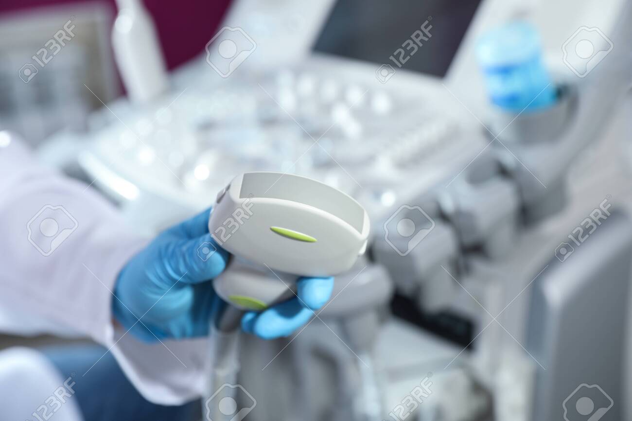 Sonographer holding ultrasound machine probe in clinic, closeup with space for text - 124147116 Sonographer holding ultrasound machine probe in clinic, closeup with space for text - 124147116