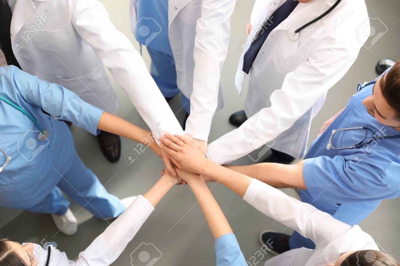 Team of medical workers holding hands together indoors, top view. Unity concept - 128765413 Team of medical workers holding hands together indoors, top view. Unity concept - 128765413