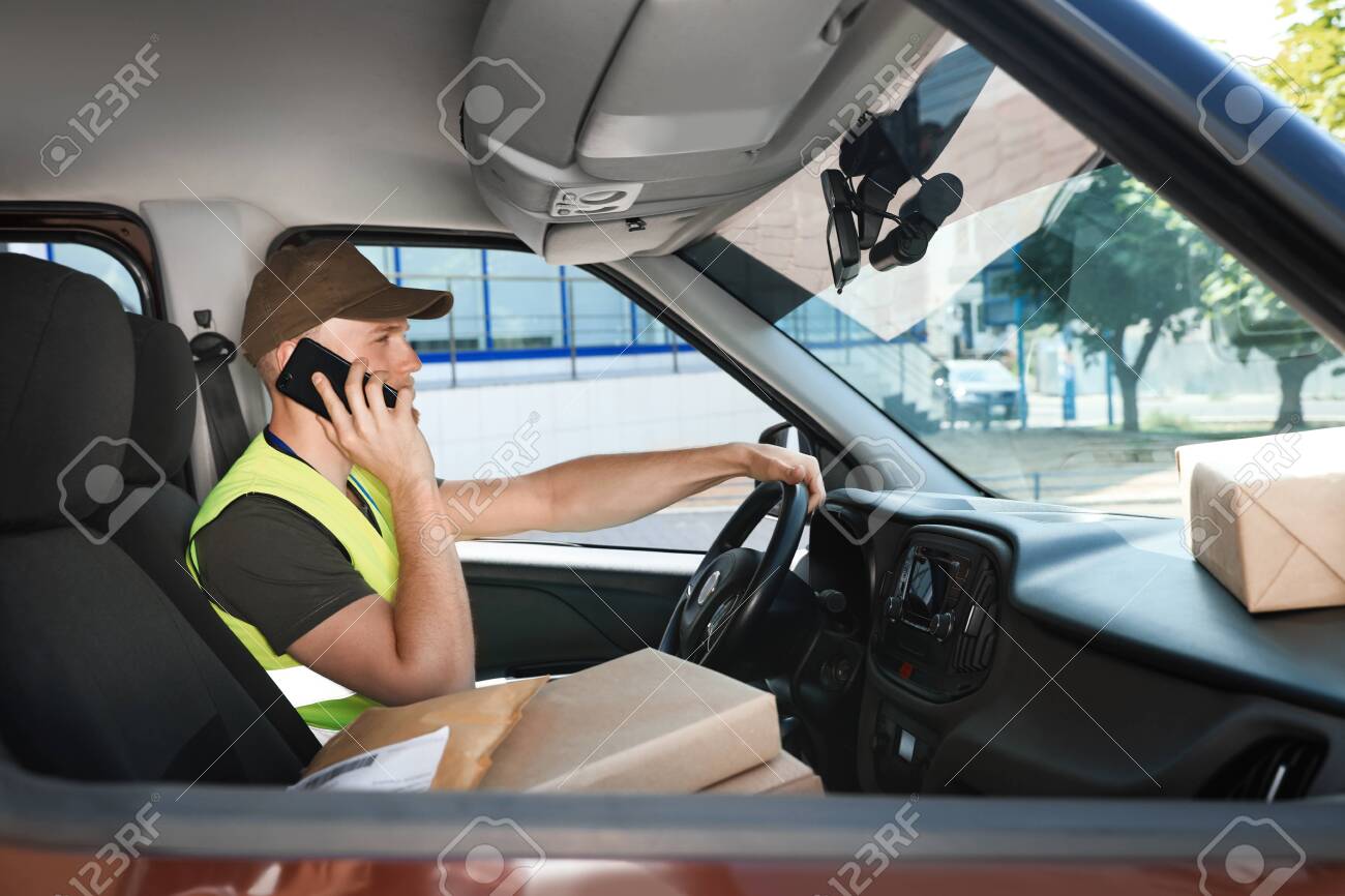 Young courier talking on phone in delivery car - 129708869 Young courier talking on phone in delivery car - 129708869