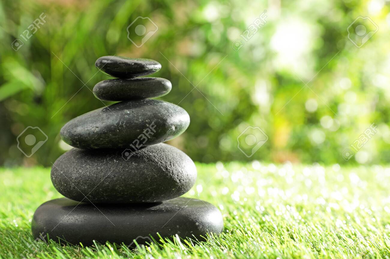 Stack of stones on green grass against blurred background, space for text. Zen concept - 130624022 Stack of stones on green grass against blurred background, space for text. Zen concept - 130624022