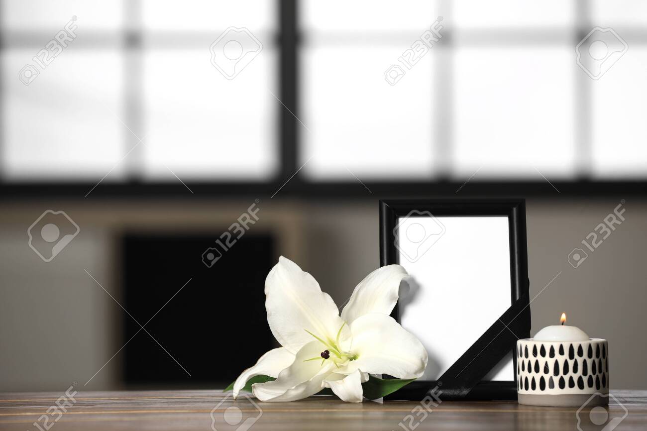 Funeral photo frame with black ribbon, lily and candle on wooden table indoors. Space for design - 132634268 Funeral photo frame with black ribbon, lily and candle on wooden table indoors. Space for design - 132634268