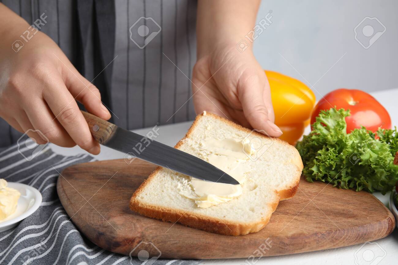Woman spreading butter on sandwich at white table, closeup - 134842305 Woman spreading butter on sandwich at white table, closeup - 134842305