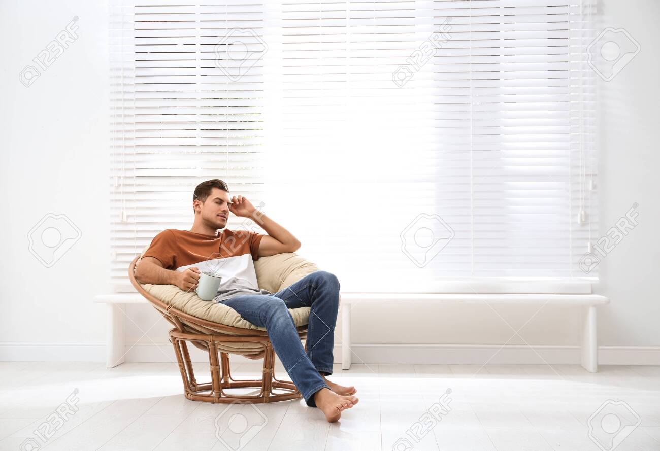 attractive man relaxing in papasan chair near window at home