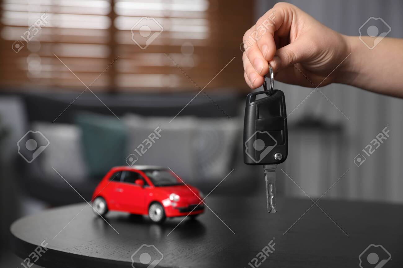 Man holding key near table with miniature automobile model indoors, closeup. Car buying - 140185531 Man holding key near table with miniature automobile model indoors, closeup. Car buying - 140185531